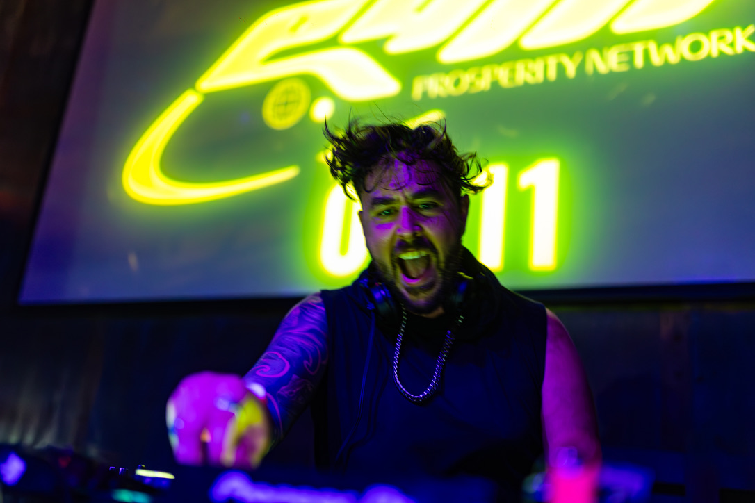 artefex performing behind the DJ decks under yellow and violet stage lighting